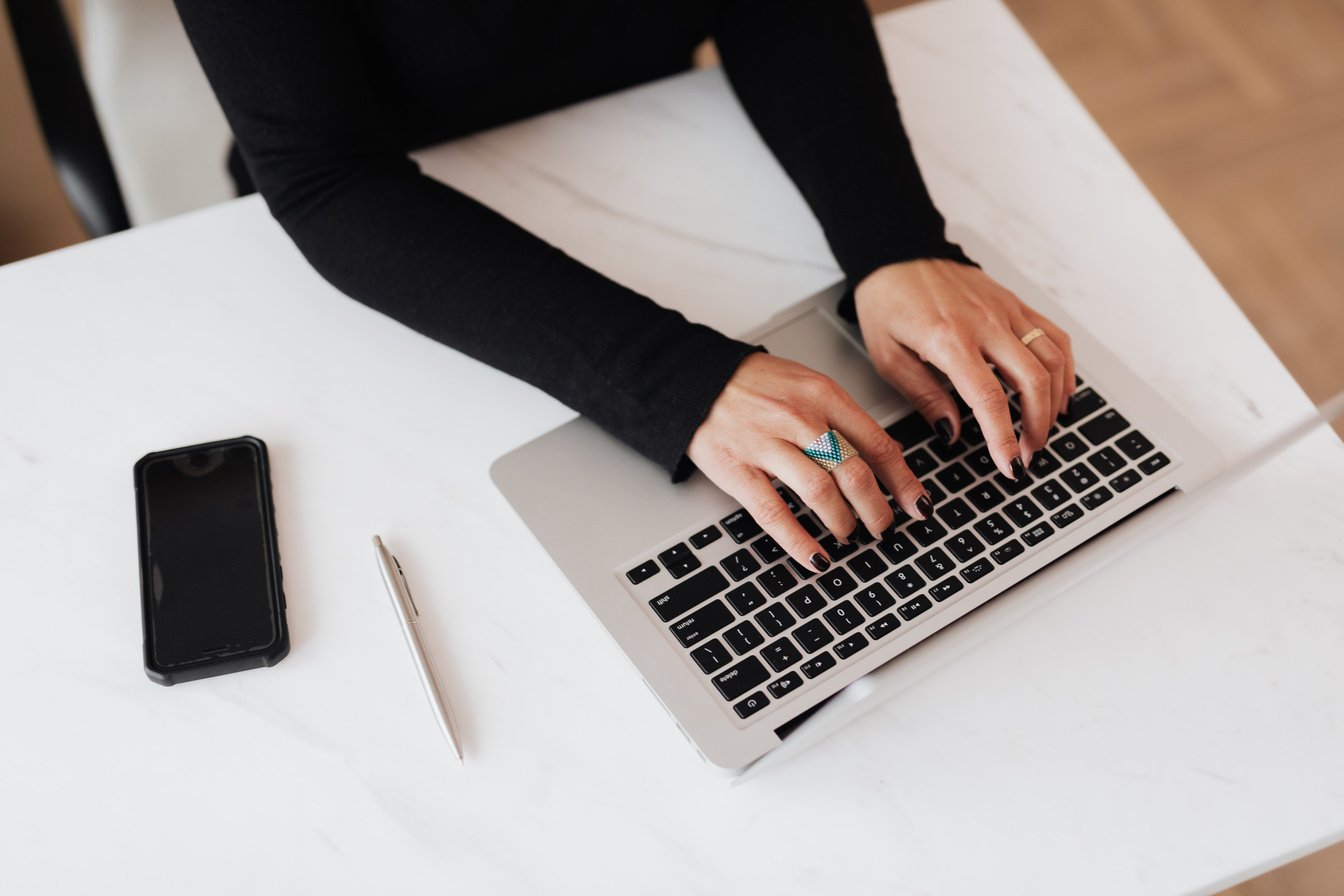 Crop faceless woman using laptop at desk in light office